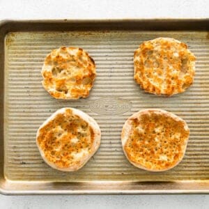4 toasted english muffins on a baking sheet.