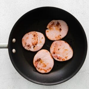 4 slices of canadian bacon in a frying pan.