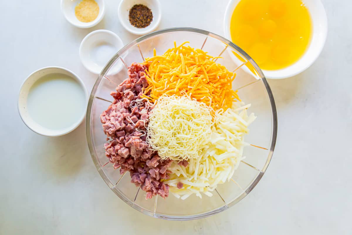 Diced ham, shredded cheese, and hash browns in a glass mixing bowl.