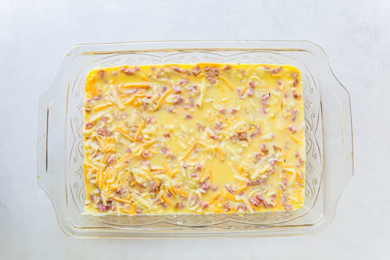 eggs poured over ham and cheese breakfast casserole ingredients in a casserole dish.