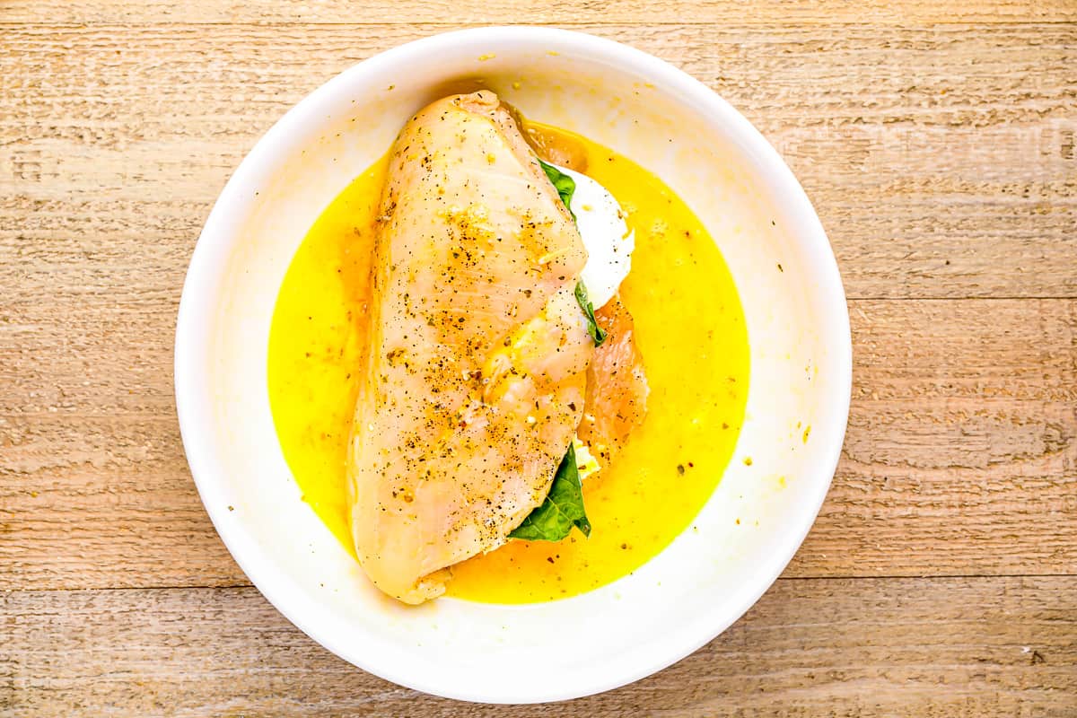 A stuffed chicken breast in a bowl of egg.