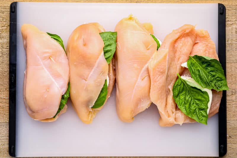 3 stuffed chicken breasts and 1 butterflied chicken breast being stuffed with mozzarella and basil.