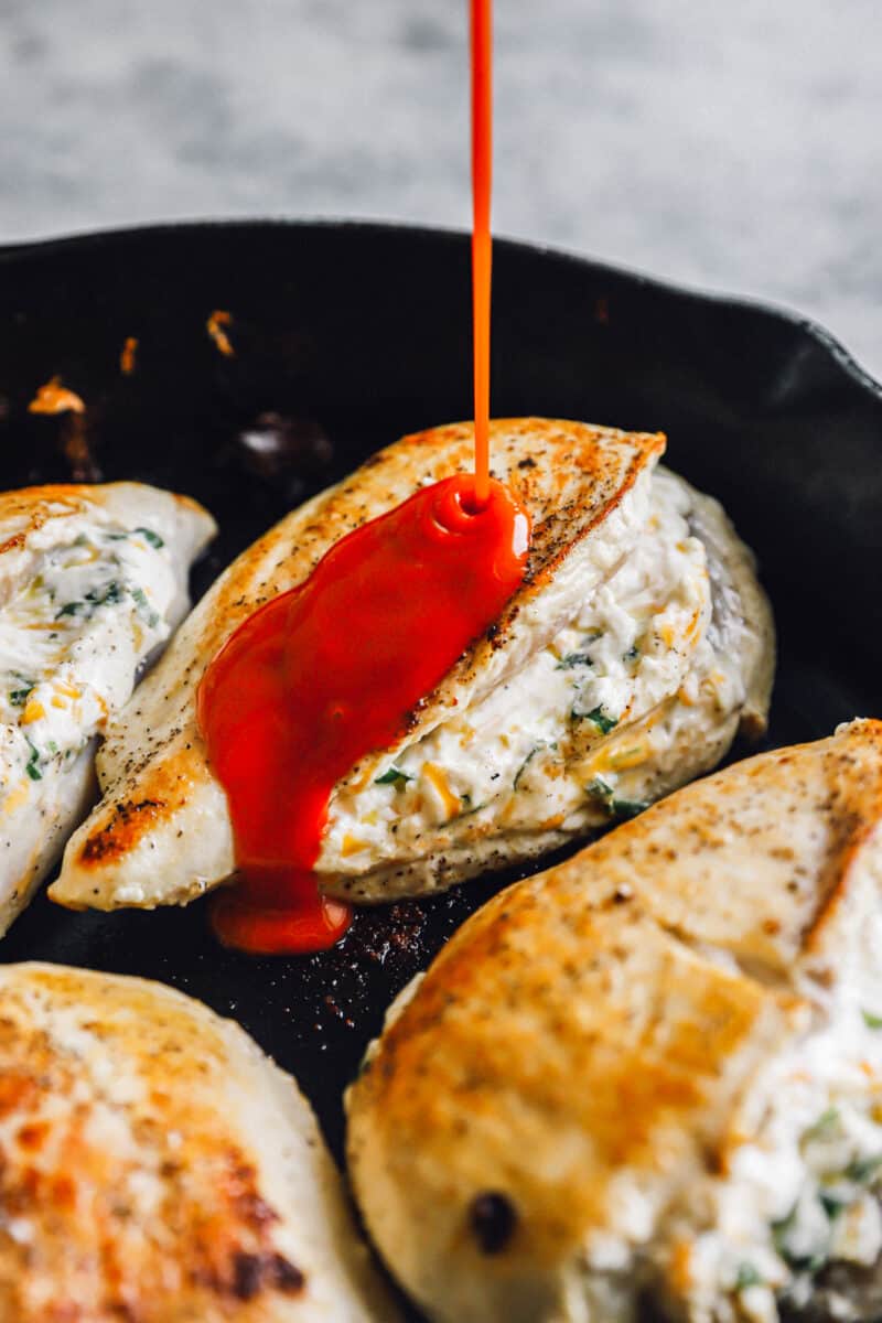 sauce poured over stuffed buffalo chicken breasts in a skillet.