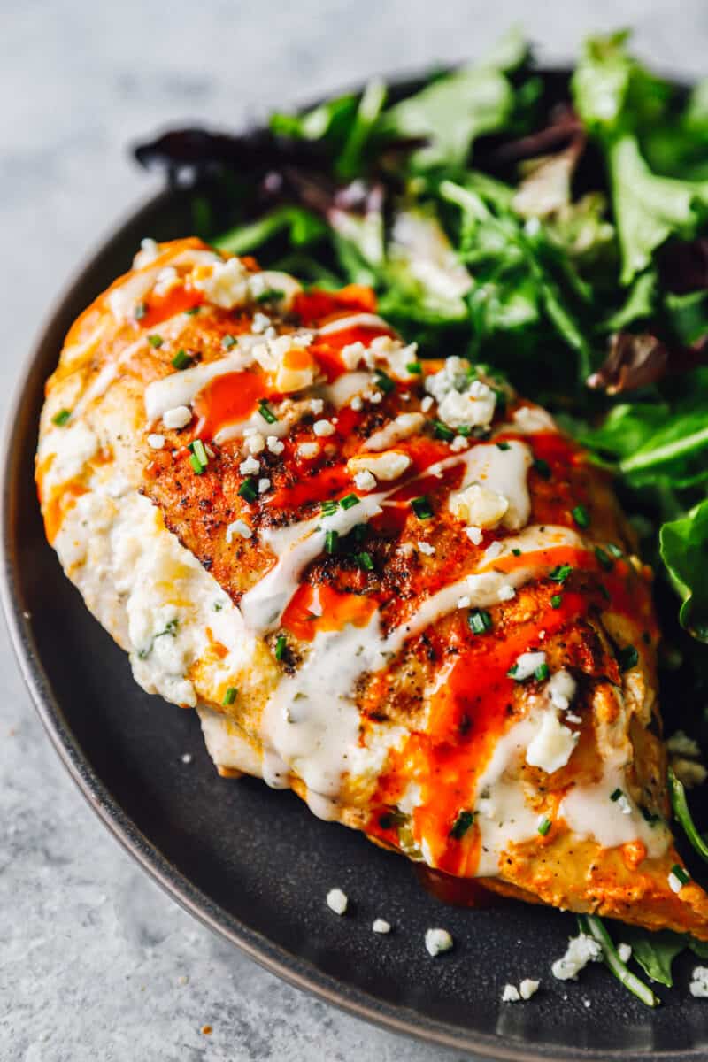 stuffed buffalo chicken breast on a black plate with salad.