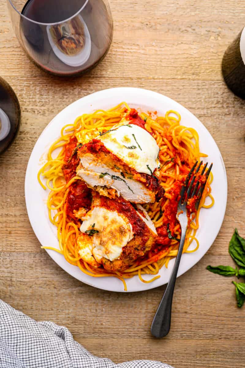 sliced stuffed chicken parmesan over pasta on a white plate with a fork.