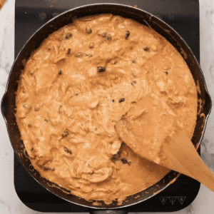 A person is stirring a skillet filled with Chicken Enchilada Dip.