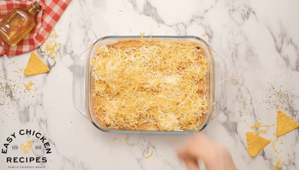 A baking dish filled with chicken enchilada dip is covered with shredded cheese. 