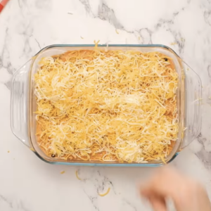 A baking dish filled with chicken enchilada dip is covered with shredded cheese.
