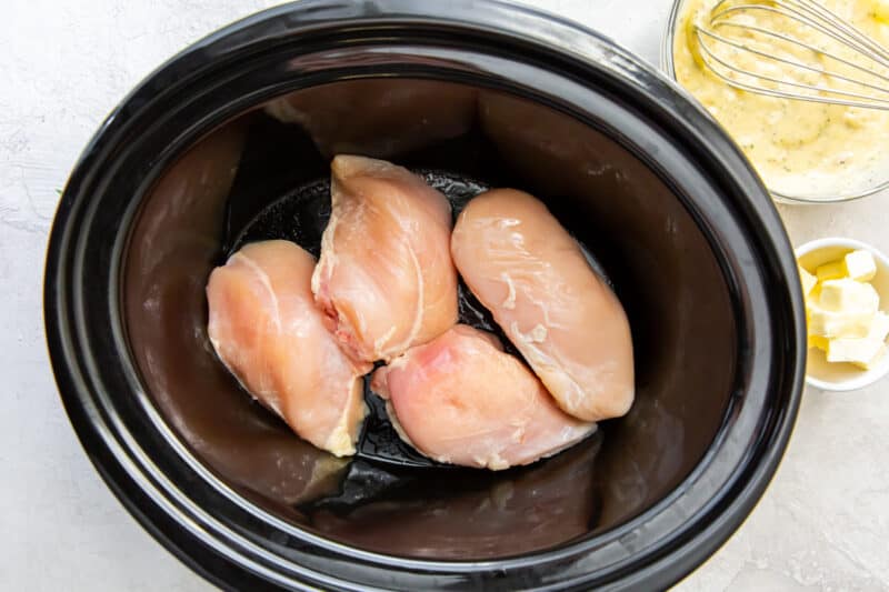 raw chicken breast in the bottom of a slow cooker