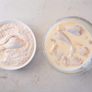 raw chicken soaking in a bowl of buttermilk, next to a bowl of seasoned flour mixture for dredging fried chicken