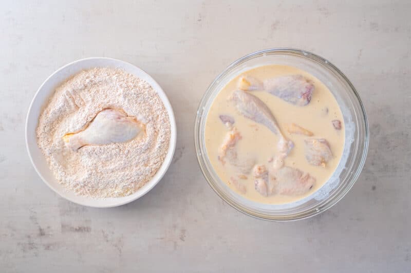 raw chicken soaking in a bowl of buttermilk, next to a bowl of seasoned flour mixture for dredging fried chicken