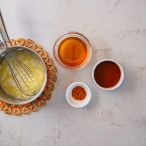 bowls of ingredients for hot honey, next to a saucepan with a whisk