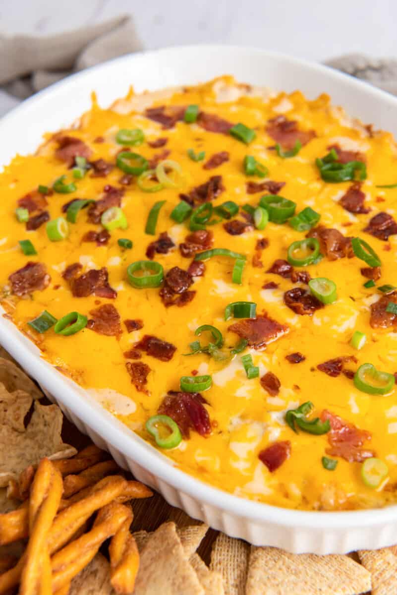 baked cheese chicken dip in a white dish, topped with bacon and green onions