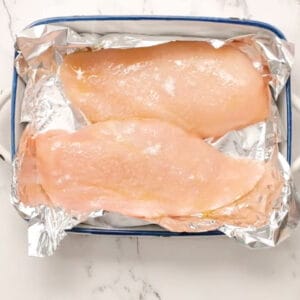 two raw seasoned chicken breasts in a foil lined pan.