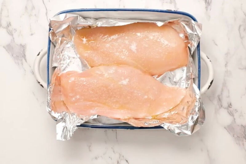 two raw seasoned chicken breasts in a foil lined pan.