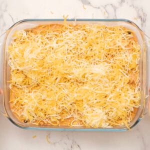 chicken enchilada dip topped with shredded cheese in a glass baking dish before baking.
