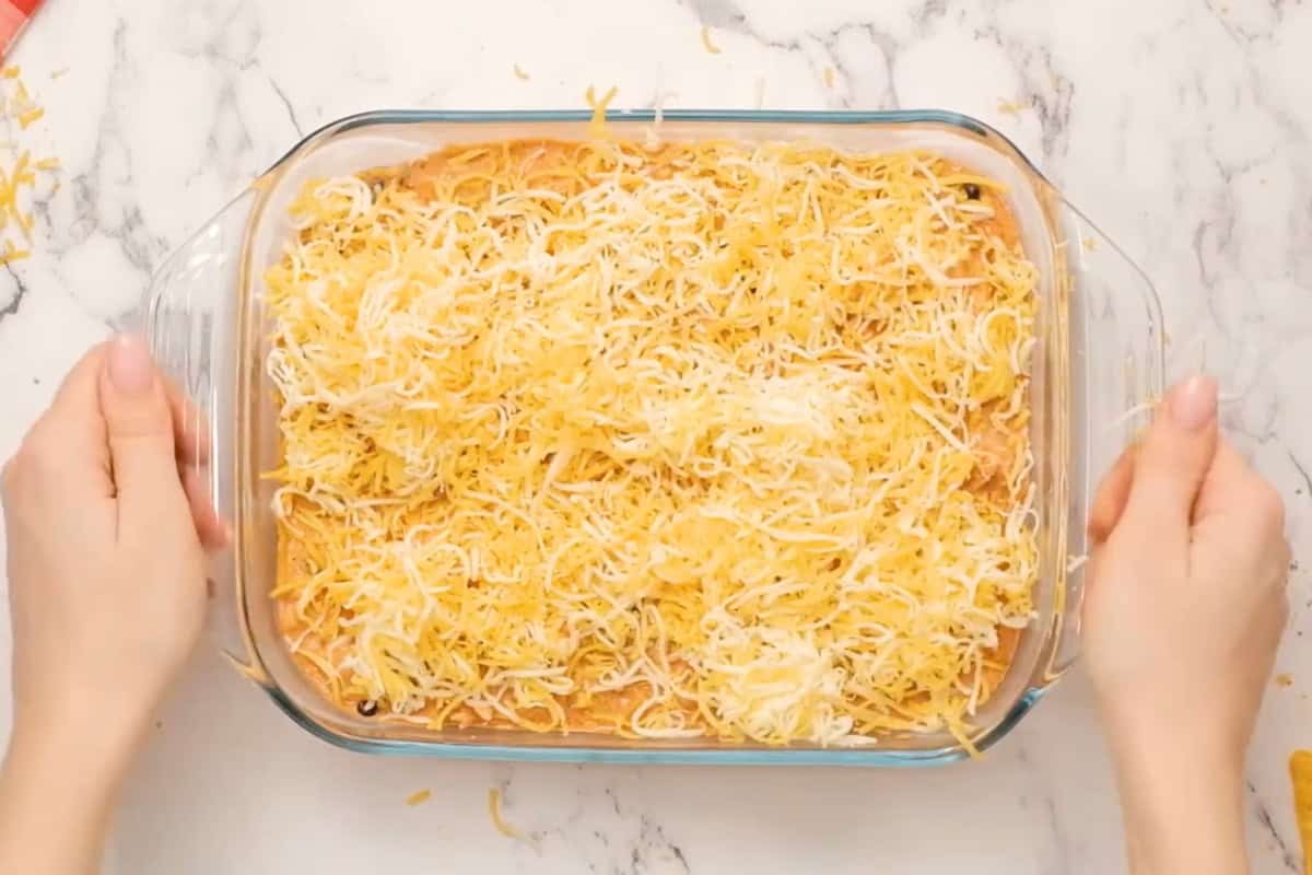 chicken enchilada dip topped with shredded cheese in a glass baking dish before baking.