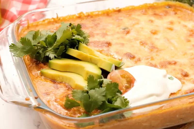 baked bubbly chicken enchilada dip topped with sour cream, tomatoes, avocado, and cilantro.
