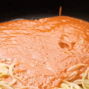 pouring enchilada sauce over sautéed onions in a skillet.