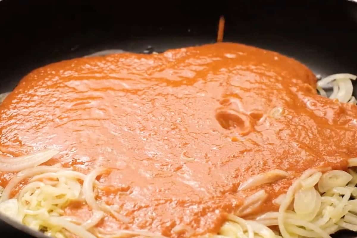 pouring enchilada sauce over sautéed onions in a skillet.