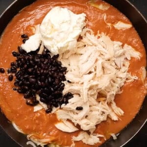 adding shredded chicken, black beans, and cream cheese to enchilada sauce in a skillet.
