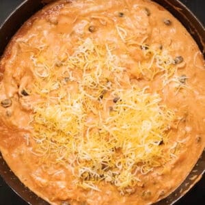 adding shredded cheese to chicken enchilada dip in a skillet.