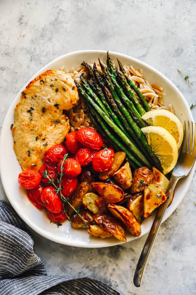 a bowl of chicken, tomatoes, asparagus, potatoes