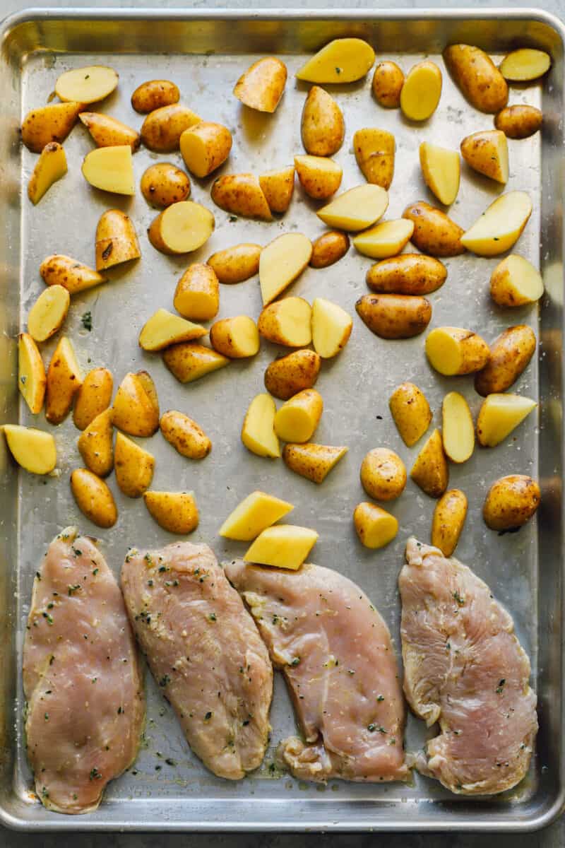 uncooked chicken breast and sliced potatoes on a sheet pan