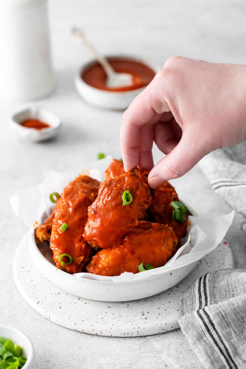 hand grabbing a chicken wing out of a bowl