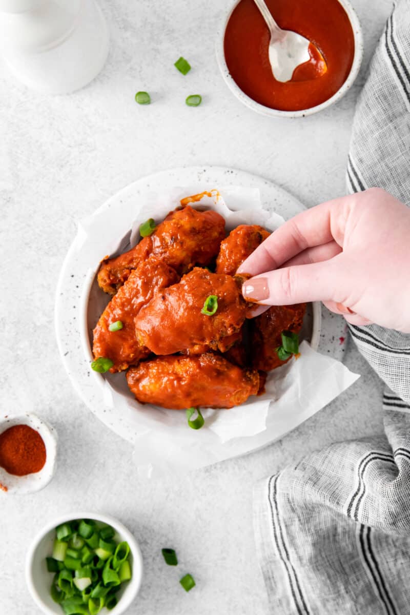 hand grabbing a hot chicken wings out of a bowl