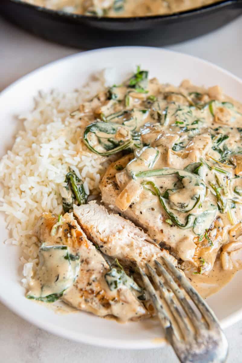 creamy chicken breast sliced up on a white plate with rice