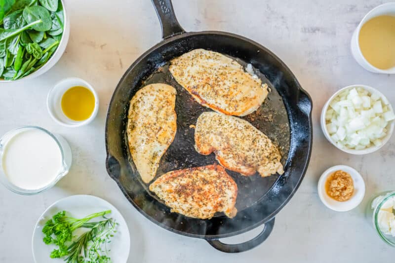 four chicken breasts cooking in a skillet