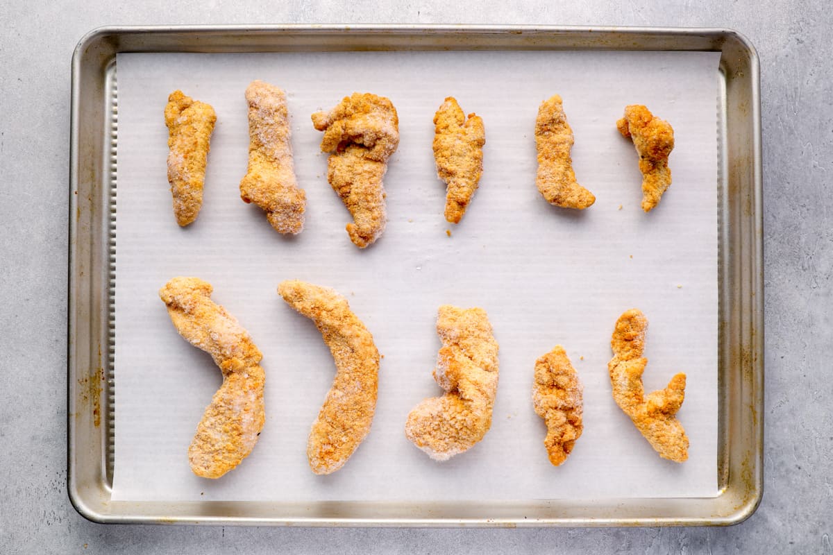 crispy chicken tenders lined up on a baking sheet