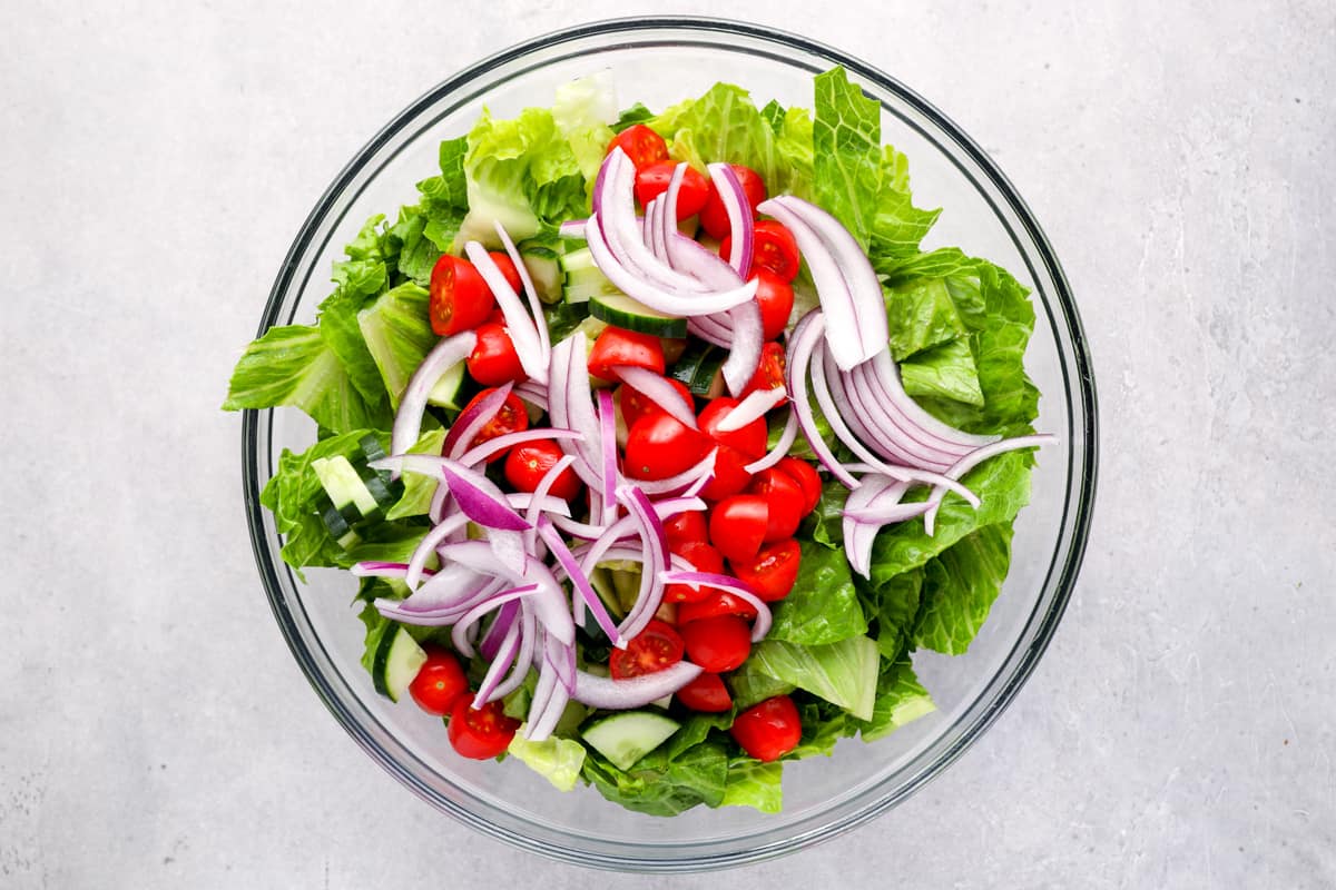 lettuce, tomatoes, and onions in a glass bowl