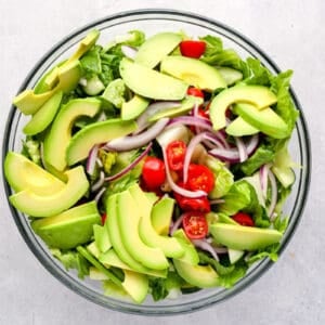 salad topped with slices of avocado in a mixing bowl