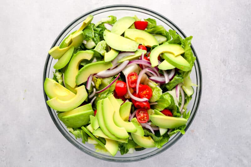 salad topped with slices of avocado in a mixing bowl