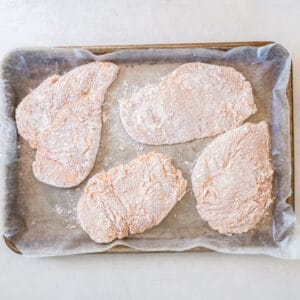 coated chicken breasts arranged on a parchment-lined baking sheet
