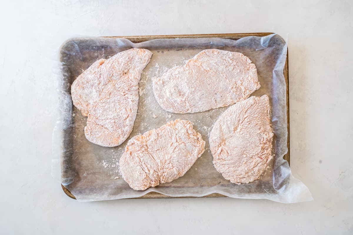 coated chicken breasts arranged on a parchment-lined baking sheet