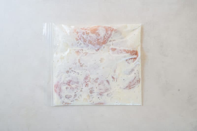 chicken breasts submerged in buttermilk marinade, inside of a sealed plastic bag