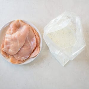 raw chicken breasts next to a bag filled with the buttermilk marinade