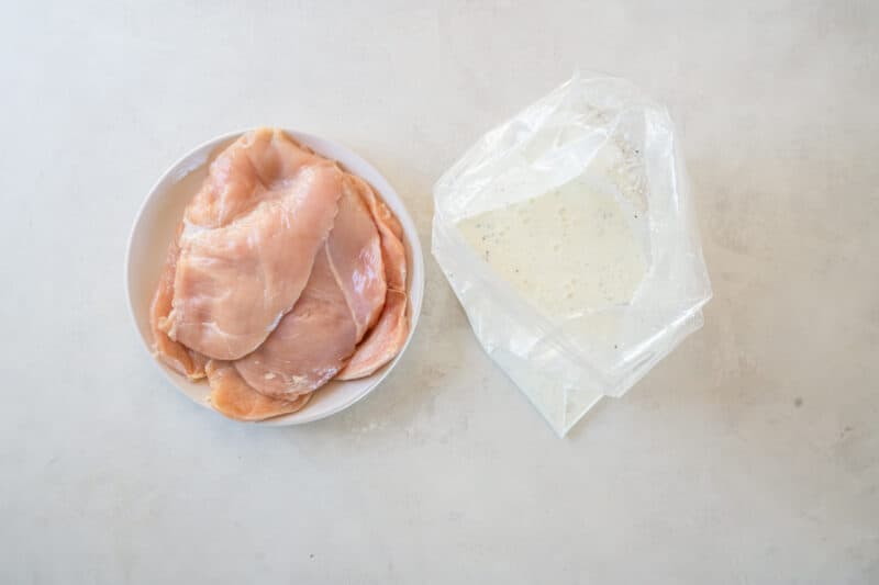 raw chicken breasts next to a bag filled with the buttermilk marinade