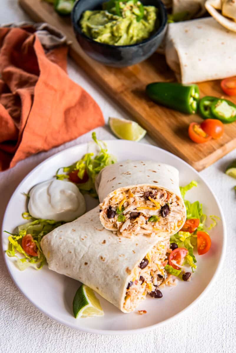 large chicken burrito cut in half, on a plate with garnish