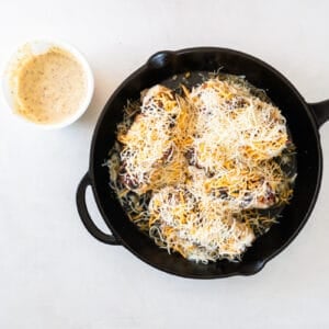 chicken breasts in a skillet, covered with shredded cheese
