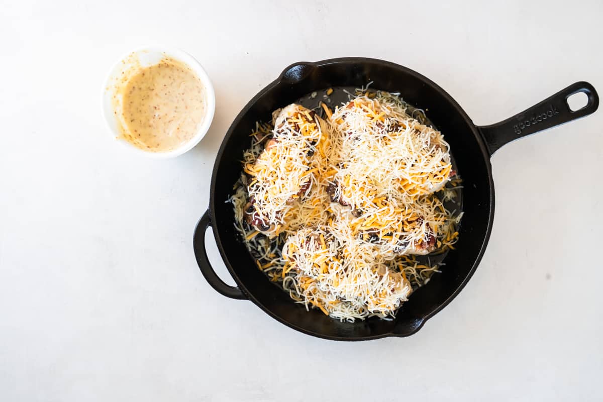 chicken breasts in a skillet, covered with shredded cheese