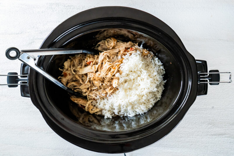 mixing shredded chicken and rice in the bowl of a crockpot