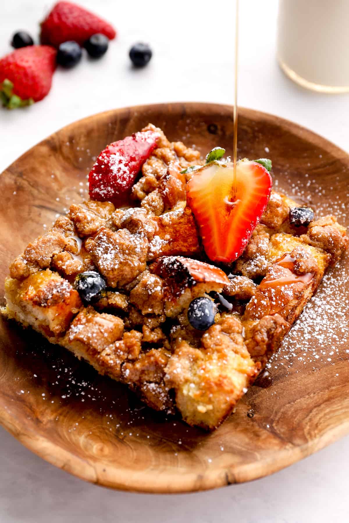 drizzling syrup on top of a slice of French toast casserole, topped with berries