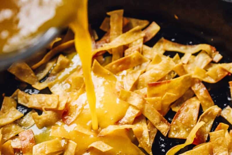 pouring egg mixture over tortilla strips in a skillet