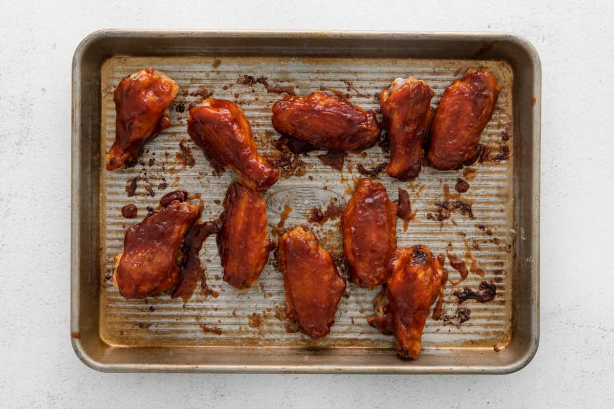 A baking tray full of chicken wings covered in Korean BBQ sauce.