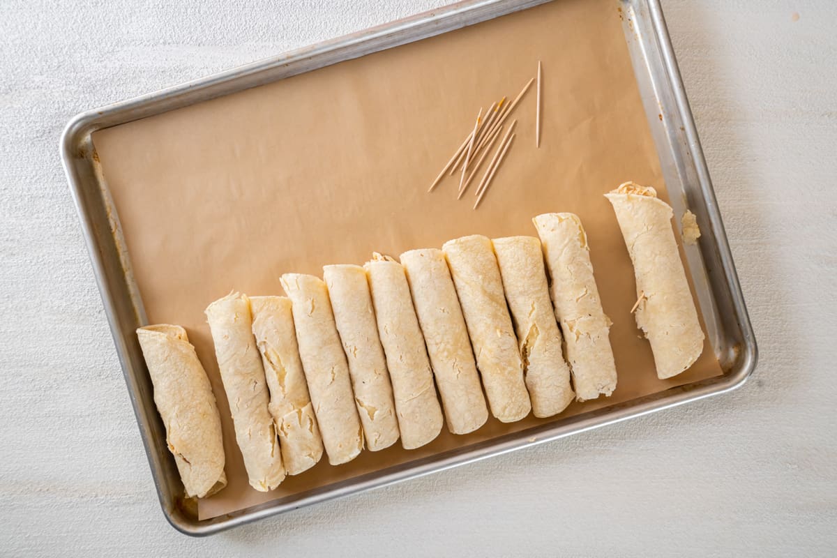 uncooked taquitos lined up on a baking tray.