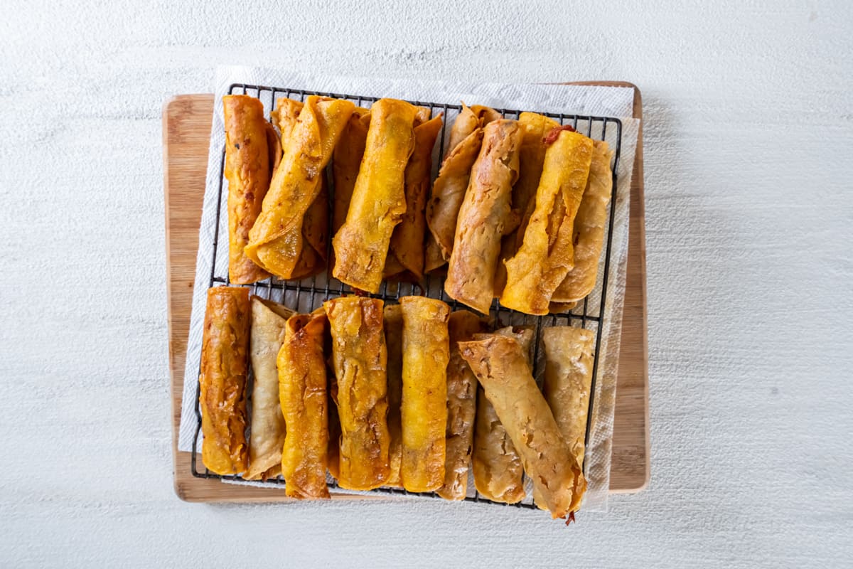 fried chicken taquitos piled up on a cooling rack.